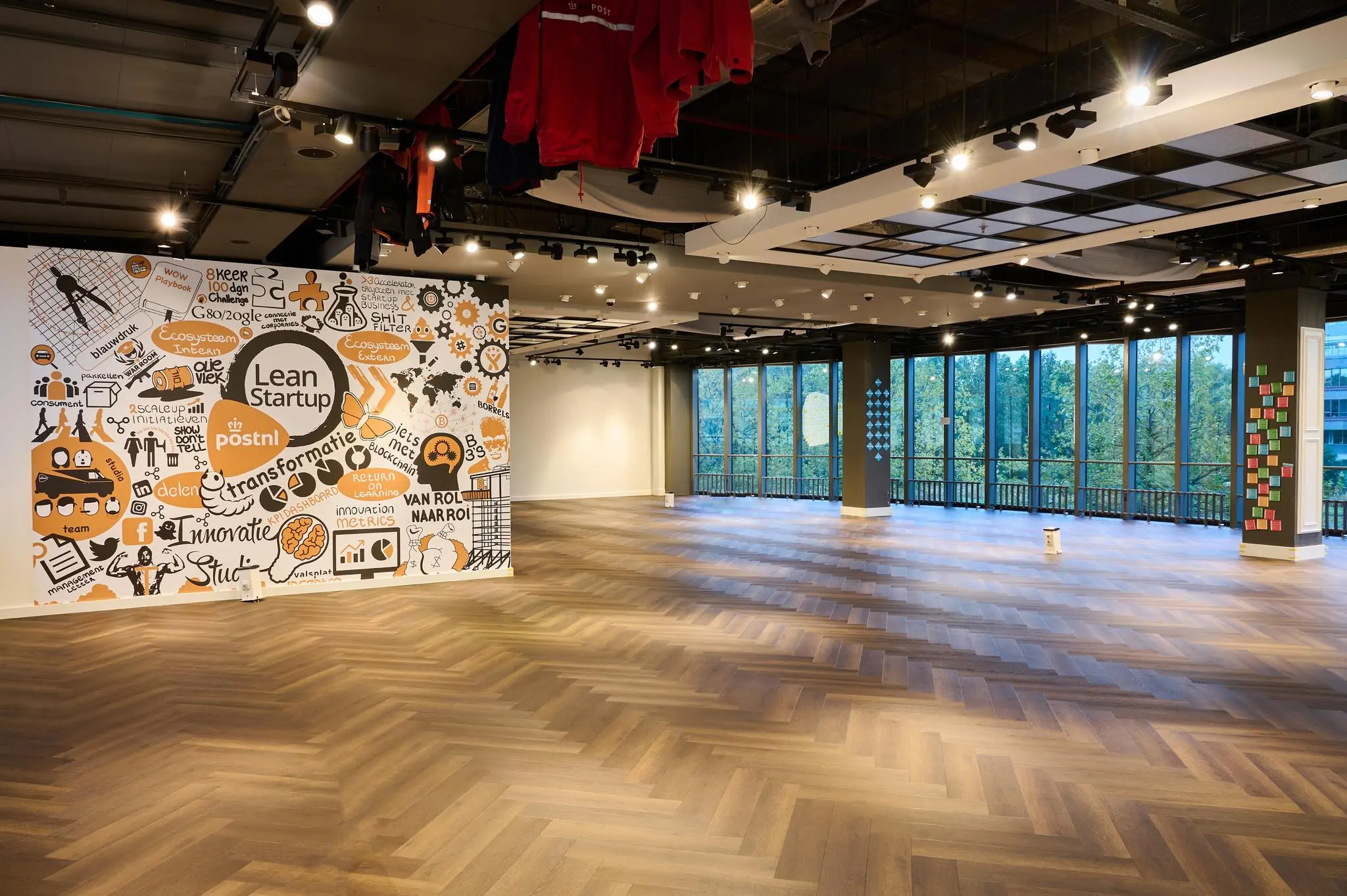 Ruime, moderne kantoorruimte aan de Johan Huizingalaan met grote ramen, houten vloer en een kleurrijke Lean Startup-muurschildering van PostNL.